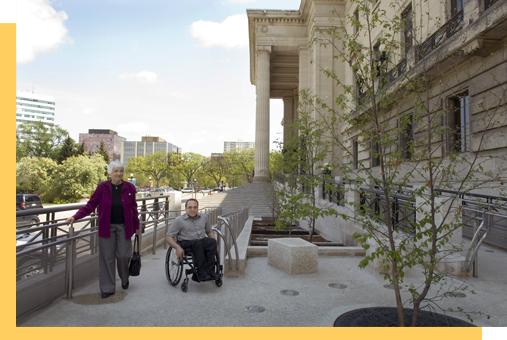 A person in a wheelchair and a person walking on the ramp at the Manitoba Legislative Building.