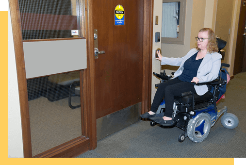 A person in a wheelchair pushing access button for a door